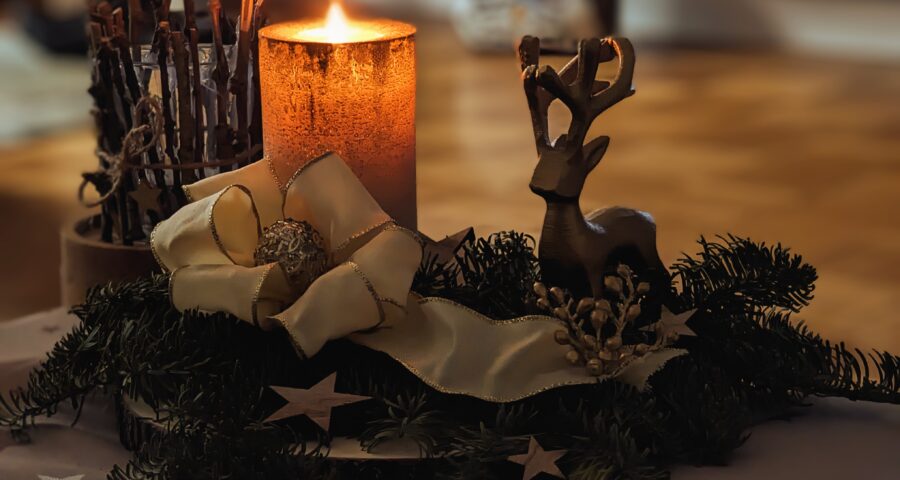 Adventsgesteck mit brennender Kerze, Tannenzweige, einem Rentier und einer Schleife.
